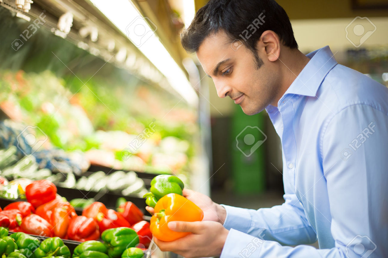 31270462-Closeup-portrait-handsome-young-man-in-blue-shirt-picking-up-bell-peppers-choosing-yellow-and-orange-Stock-Photo